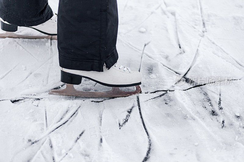 冰鞋的特写照片。White figure skating skates, person learns to ride them on ice of frozen lake in winter